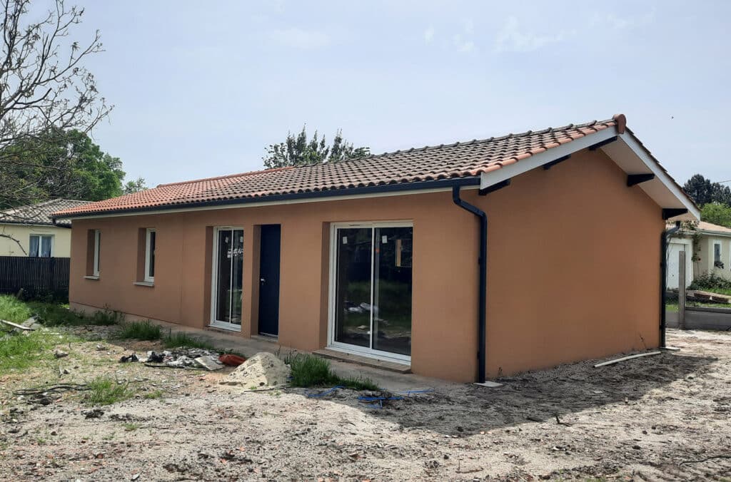 Maison moderne de plain-pied avec façade orange, grandes baies vitrées et toiture en tuiles romanes.