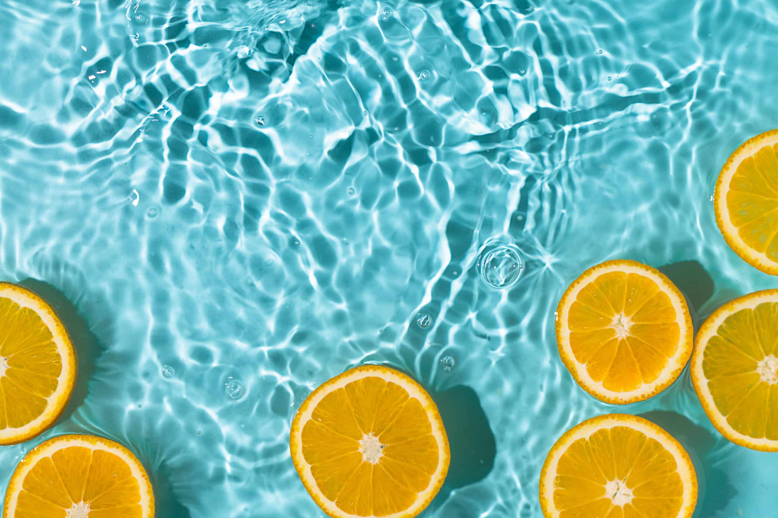 Tranches d'oranges fraîches flottant sur une eau bleue turquoise ondulée avec des reflets lumineux cristallins.